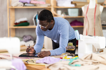 Fototapeta premium Male tailor draws sketch of future clothing on an electronic tablet. Working with modern gadgets in a sewing workshop