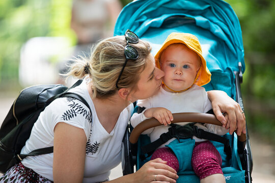 Loving Mother Kissing Her Baby in a Stroller Outdoors