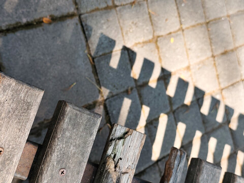 High angle view of wooden bench backrest casting geometric shadow pattern on stone floor