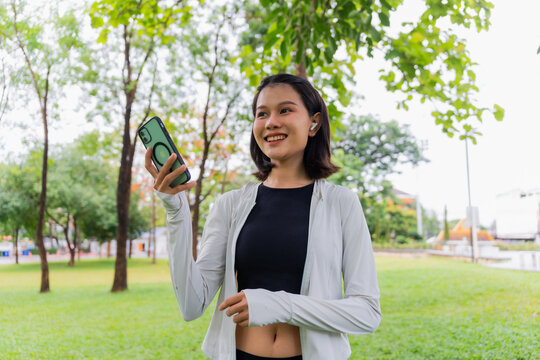 Asian sporty woman using earphone listen to music on smartphone in public park