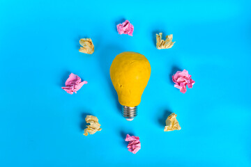 Yellow light bulb surrounded by crumpled colorful paper balls on bright blue background  © kaliel