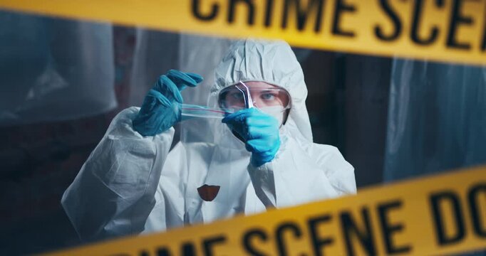 Forensic investigator carefully collects trace evidence into a sealed evidence bag behind crime scene tape during a criminal investigation.