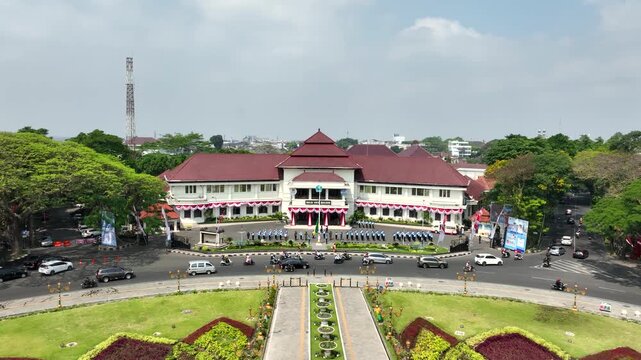 Forward aerial footage of historic Malang City Hall in East Java, Indonesia, with youth scout units performing a flag practice session outside the colonial landmark.