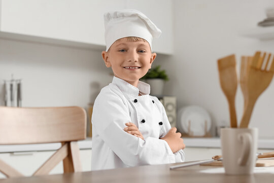 Smiling young boy in a chefs uniform with arms crossed culinary education and cooking hobby in a modern kitchen
