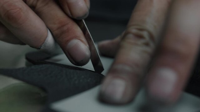 Hands carefully cutting leather pieces for shoes with a knife in a workshop setting