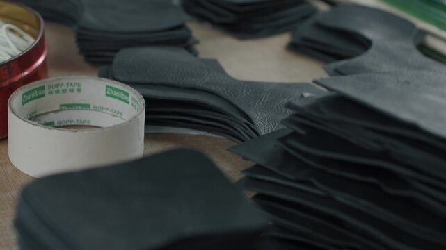 Stacks of cut leather shoe pieces arranged on a workbench in a factory setting
