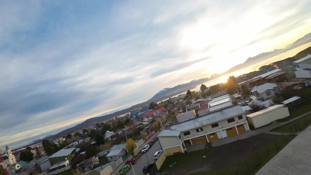 Running track and soccer field of Estadio V&iacute;ctor B&oacute;rquez Miranda alongside colorful rooftops and distant mountains in Puerto Natales, Chile, FPV aerial