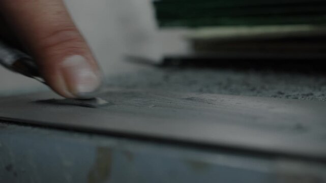 Close-up of worker hand cutting material with utility knife in shoe production process