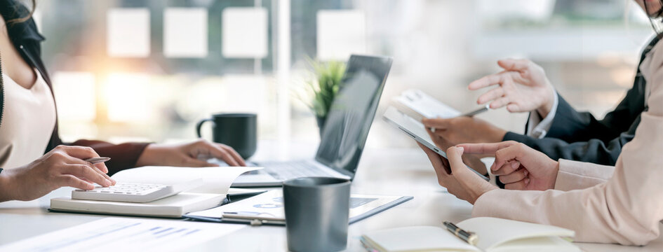 Professional business team discussing work with tablets, laptop, and calculator in banner size