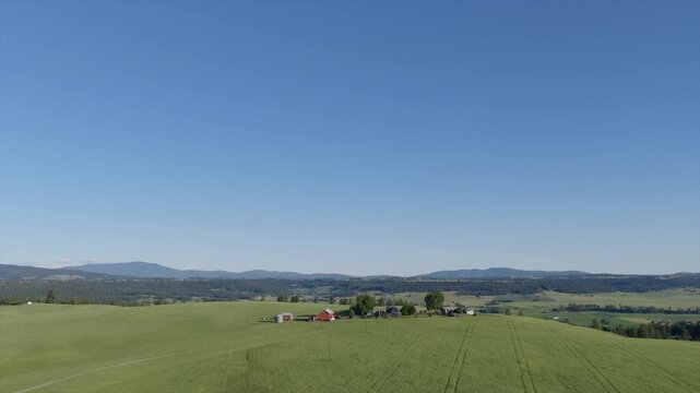 Wide aerial view of a farmhouse and outbuildings set among green fields, with mountains stretching along the Spokane, WA horizon.