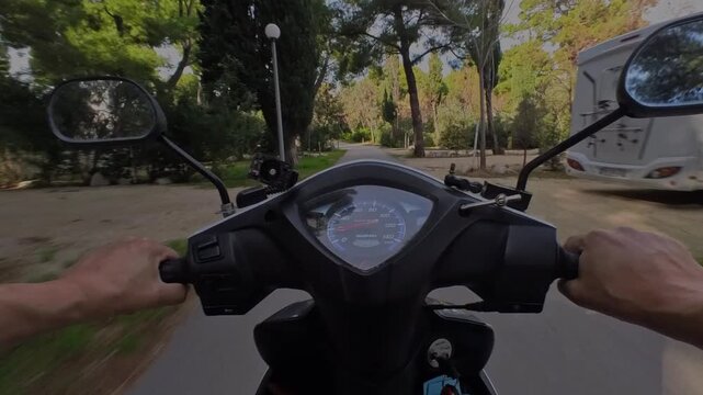 POV shot riding a scooter on road surrounded by green trees. Concept for moped rental, summer travel, freedom, two wheel transport, and outdoor commuting