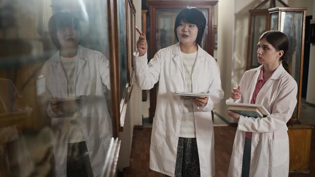 Asian and Caucasian young adult female medical students in lab coats standing in anatomy museum, discussing specimens. Clip suitable for medical education and university marketing campaigns