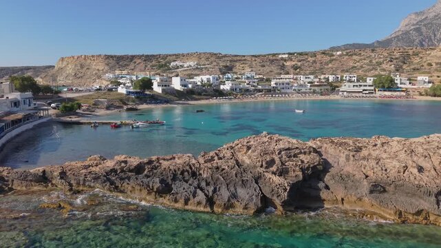 Lateral drone shot of Lefkos Beach in Karpathos, capturing beachfront restaurants, sunbeds, crystal-clear waters, and the relaxing atmosphere of this popular seaside destination.