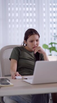 Stressed young Asian woman showing frustration while working on laptop at home office desk