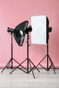 Professional studio lighting equipment with a softbox and strobe light on tripods against a pink background, the setup is positioned against a vibrant pink background with a light grey wooden floor