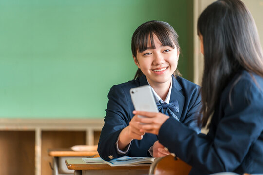 A middle school girl talking while looking at her smartphone in a school classroom.