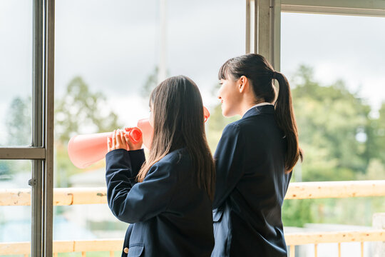 Women (students, junior high school girls, high school girls) cheering from classrooms and school buildings with megaphones.