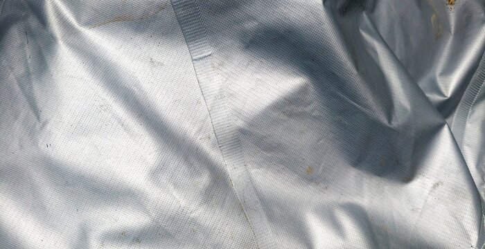 Wrinkled gray canvas background. close-up photograph of a crinkled, metallic silver foil or tarpaulin material displaying a finely textured grid pattern. The surface shows soft light reflections