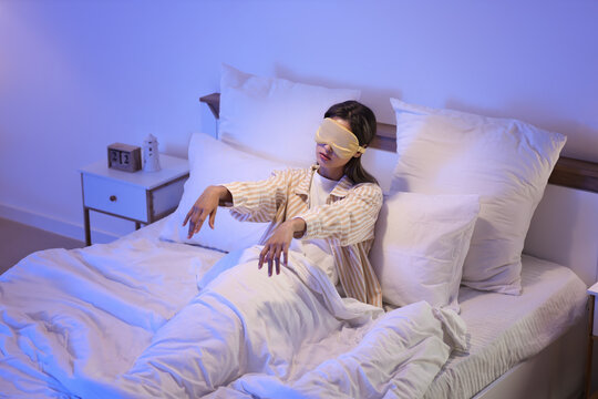 Female sleepwalker with sleeping mask lying on bed in bedroom at night