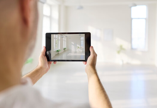 Designer man with tablet photographs bright interior. Tablet screen shows the room and hall, a photo aiding planning and renovation using modern technology. Digital tools for interior planning.