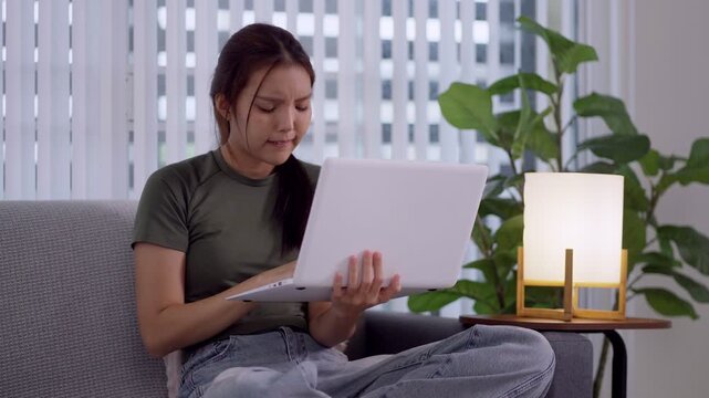 Stressed young Asian woman experiencing headache and frustration while working on laptop at home