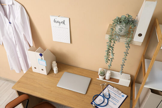 Doctors workplace with laptop and flip calendar on beige wall in medical office