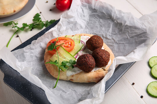 Baking dish of delicious pita with falafel and fresh vegetables on white wooden background, closeup