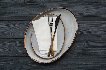 Obraz premium Plates with cutlery and paper napkins on black wooden background
