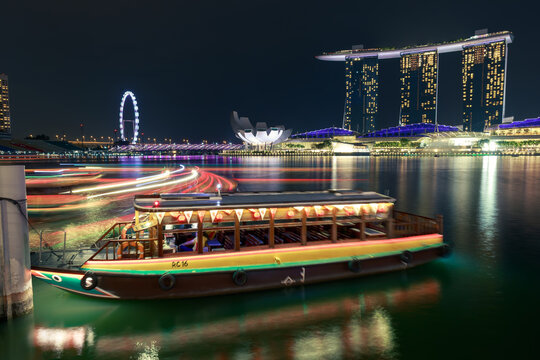 Long exposure night view of Marina Bay Sands, Singapore Flyer and the Marina Bay waterfront with colorful boat light trails reflecting on the calm water in Singapore