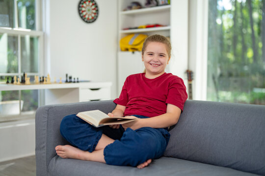 Clever child reading a book at home. Clever kid read book in a home interior. Clever reader enjoying a story books at home. Clever kid reading book and learning in the playroom. Child holding a book.