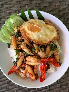 Spicy Basil Crab with Fried Egg: A delicious plate of spicy basil crab served over rice, topped with a perfectly fried egg and garnished with fresh cucumber slices.