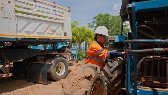 Asian technician worker fixing heavy machinery tractor engine at construction or farm site. Professional industrial mechanic service, vehicle maintenance and troubleshooting inspection.