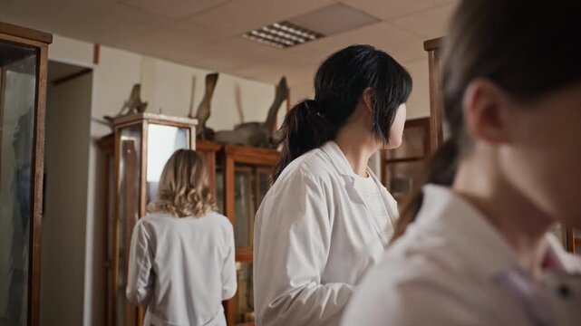 Asian and Caucasian young adult female medical students wearing lab coats studying anatomical specimens in museum, taking notes. Video is perfect for medical school advertising