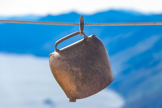 Traditional swiss cowbell hanging on a steel wire rope fencing with a blurred alpine mountain background