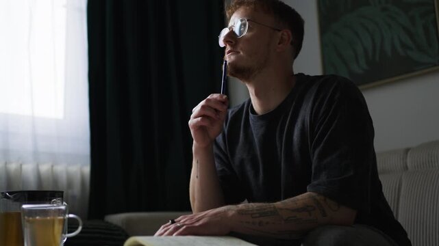 Focused young person writes journal or goals at home desk, cup nearby