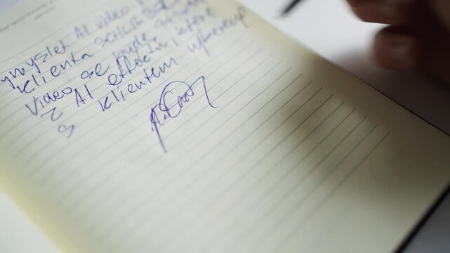 Close-up of person writing signature on lined paper with text above.