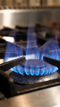 Blue Gas Flame on Stove Burner - A close-up shot captures vibrant blue flames igniting from a gas stove burner. The intense blue flames rise from the metal grate, creating a dynamic and fiery visual.