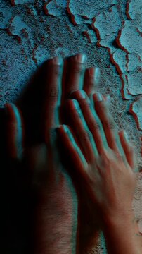 Close-up of Hands Touching Textured Wall Under Colorful Light - Two hands, one larger and one smaller, gently touch a rough, textured wall.