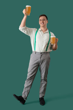 Handsome young happy man in traditional German clothes with mugs of beer on green background