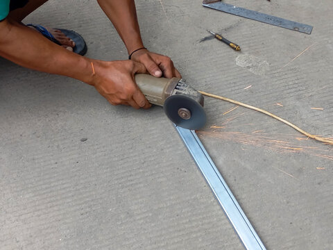 Worker cuts metal using an angle grinder tool outdoors.