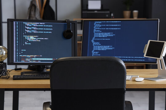 Computer monitors with programming code and headphones on desk in office