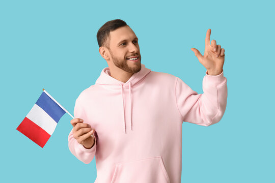 Young man with flag of France pointing at something on blue background