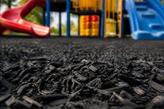 Black rubber playground surface with colorful play equipment in the background.