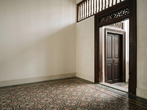 Empty room corner with Peranakan tile floor and carved wood door