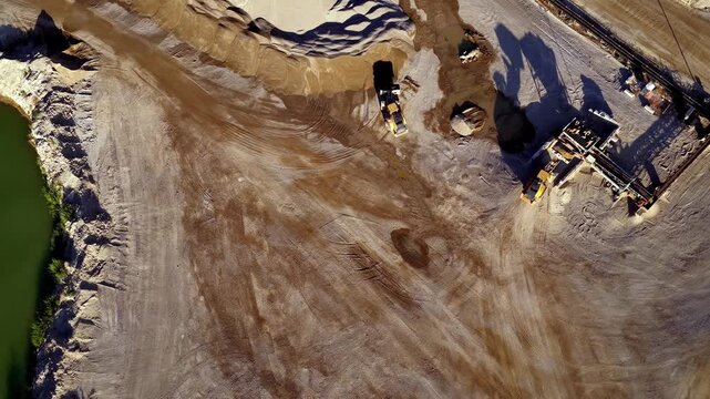 Drone aerial footage shows wheel loaders operating at a busy aggregate gravel and sand pit, moving raw materials under bright sunlight. Static, straight down view.