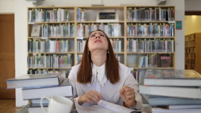 Young woman feels overwhelmed by difficult studying in a library as piles of books and endless reading leave her frustrated exhausted and desperate for a break once again