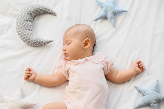 Little cute baby with toys sleeping on bed at home