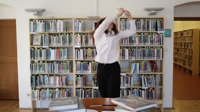 Happy university student celebrates passing a difficult exam in library holding a book after intense studying and feels proud relieved excited about her academic success