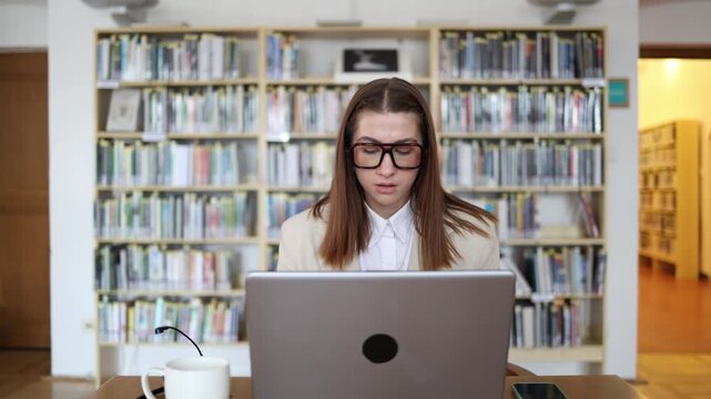 Graduate student concentrates on writing her final thesis on laptop in a library organizing research findings and completing academic work before an important deadline