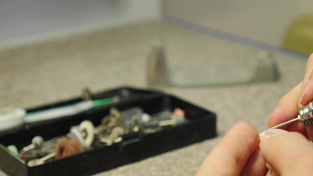 Close-up of skilled technician hands shaping ceramic dental crown with rotating handpiece. Blurred bur box and reflection on workbench glass. Professional laboratory crafting procedure 4k video